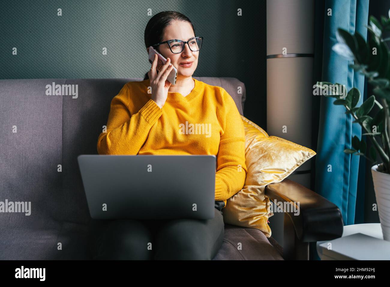 Portrait d'une femme d'affaires confiante en lunettes, assise sur un canapé, téléphone parlant près de l'usine, travail distant, Banque D'Images