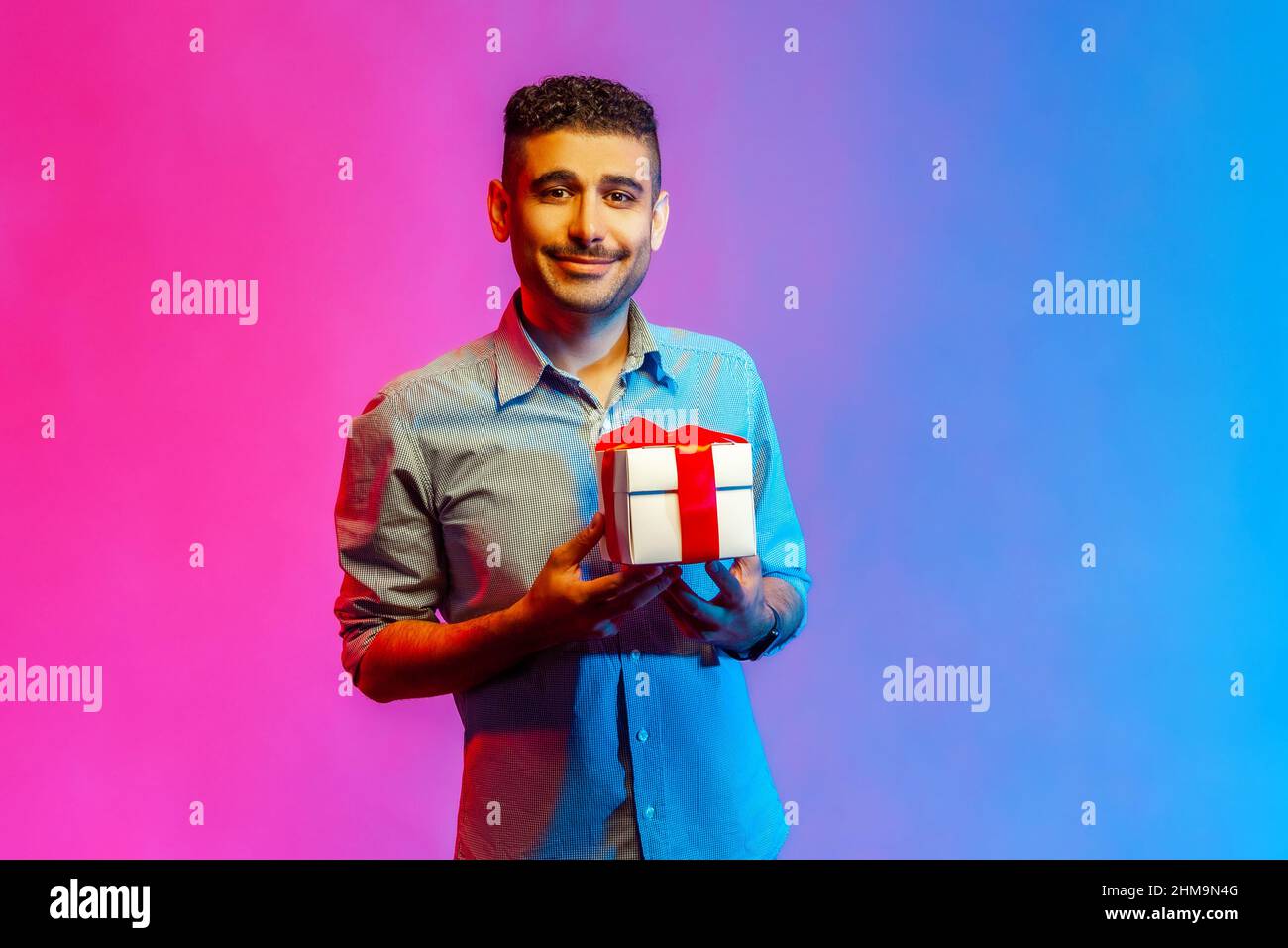 Portrait d'un homme souriant et souriant dans une chemise tenant un cadeau  et regardant un appareil photo avec un sourire crasseux, des cadeaux et des  bonus, la célébration. Studio d'intérieur isolé sur