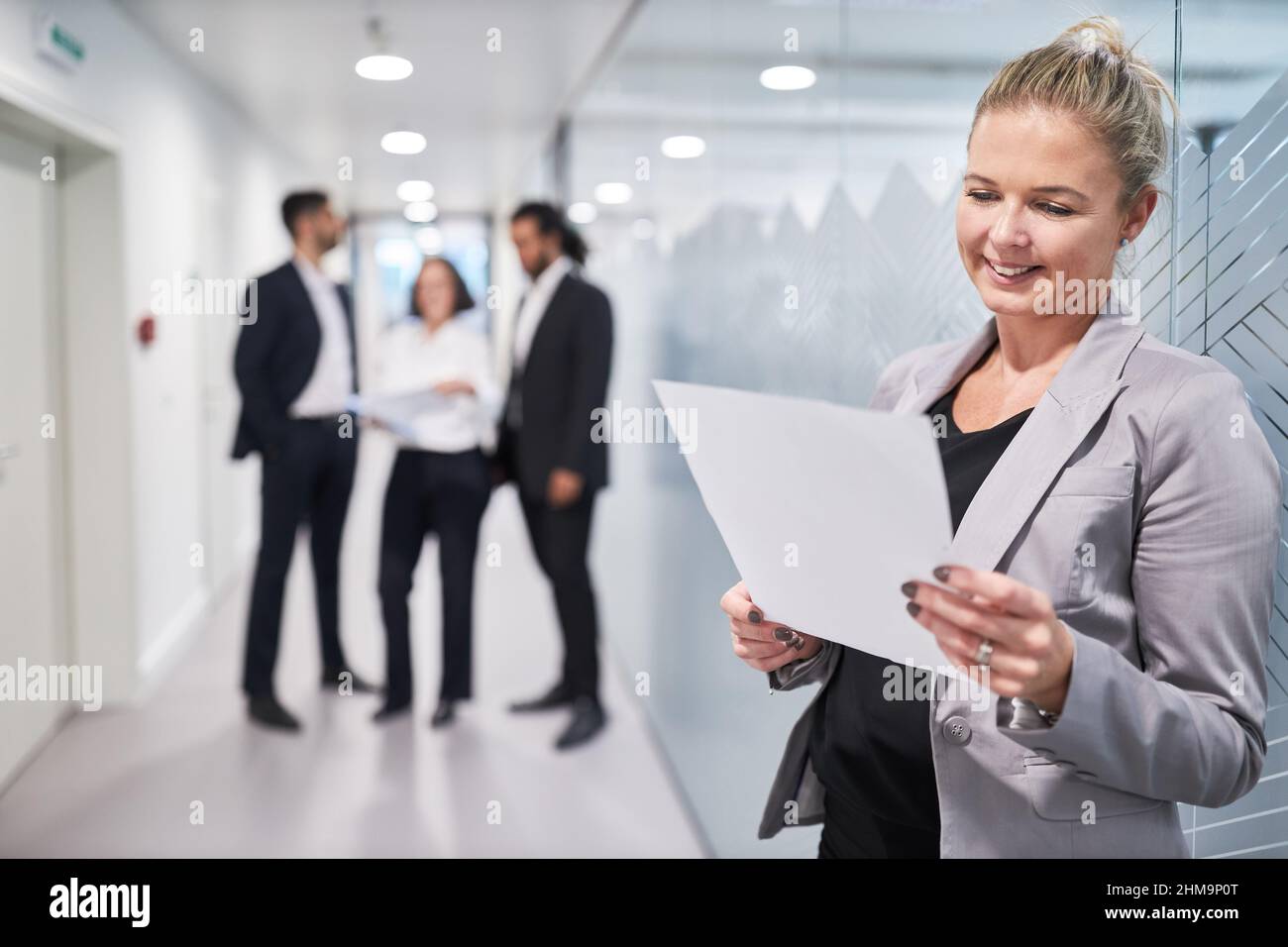 Femme d'affaires satisfaite lisant un contrat ou un bon de commande dans le couloir depuis le bureau Banque D'Images