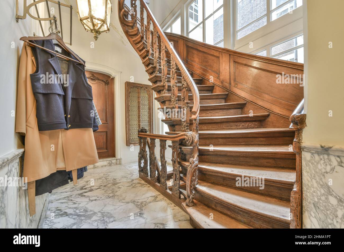 Escalier en bois avec balustrade ornementale placé dans le couloir avec des vêtements accrochés sur un rack dans un appartement lumineux avec des fenêtres à la maison Banque D'Images