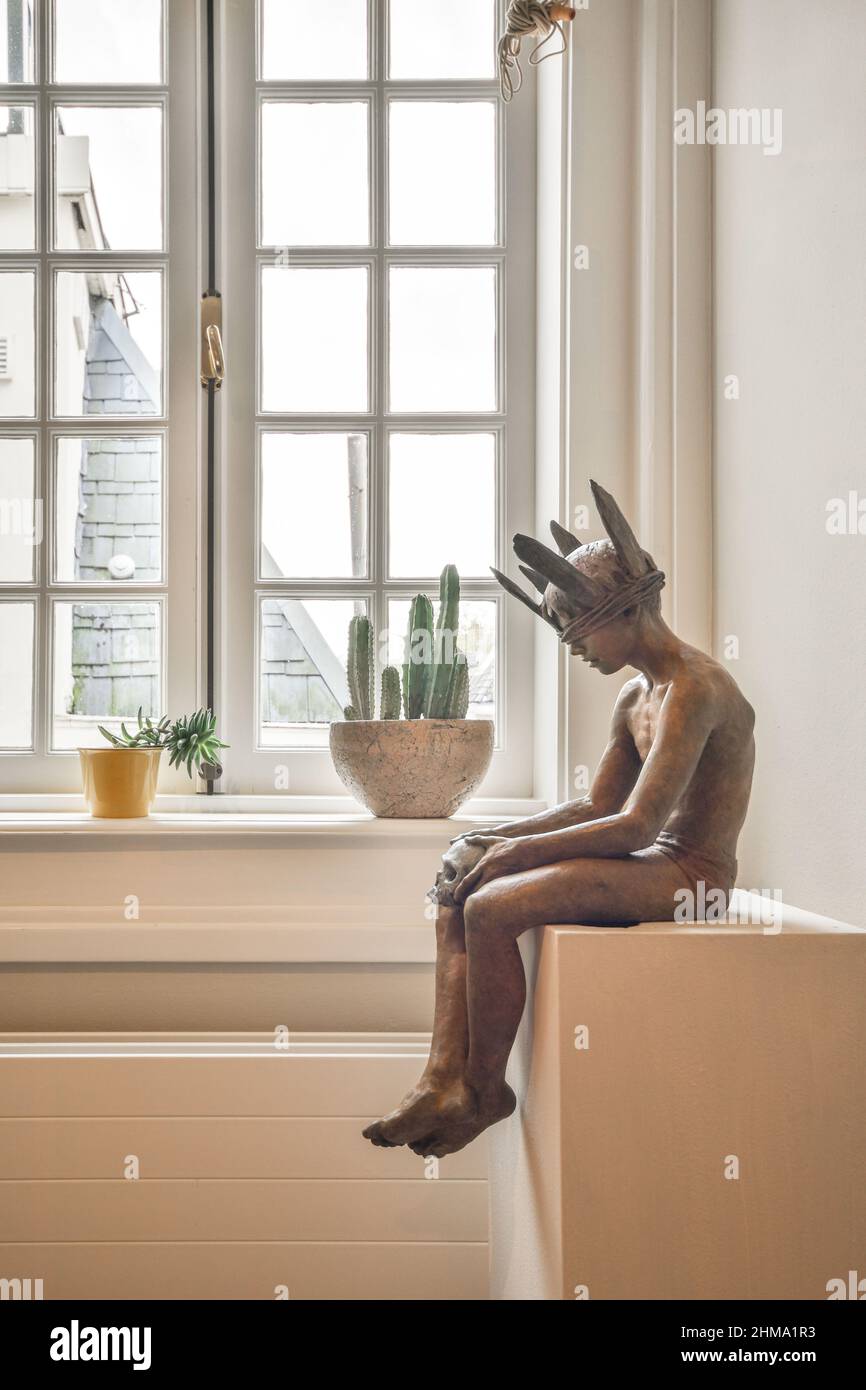 Statue de l'homme dans la couronne placée sur le cabinet blanc près des plantes vertes en pot à la fenêtre dans la pièce lumineuse à la maison Banque D'Images
