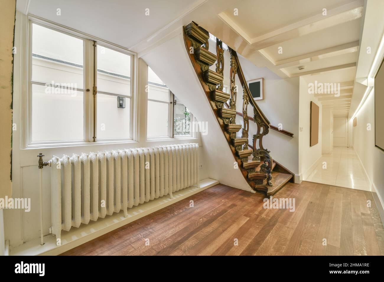 Escalier avec rambardes ornementales placé près de la fenêtre et des radiateurs dans appartement lumineux spacieux avec couloir long et cadres décoratifs à la maison Banque D'Images