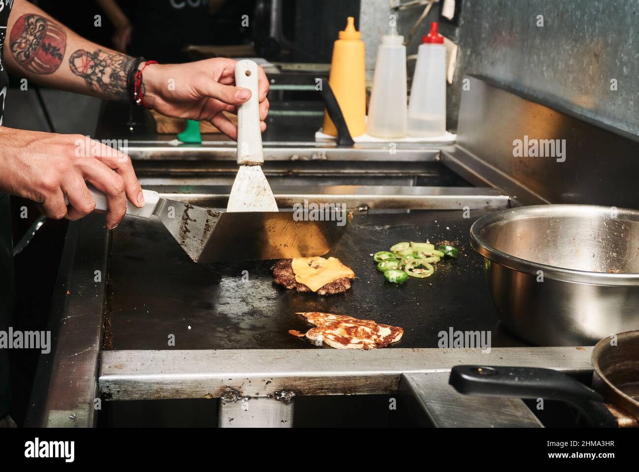 Vue latérale de la récolte non reconnaissable faire cuire la friture et retourner les côtelettes de hamburger avec des spatules dans un camion alimentaire Banque D'Images