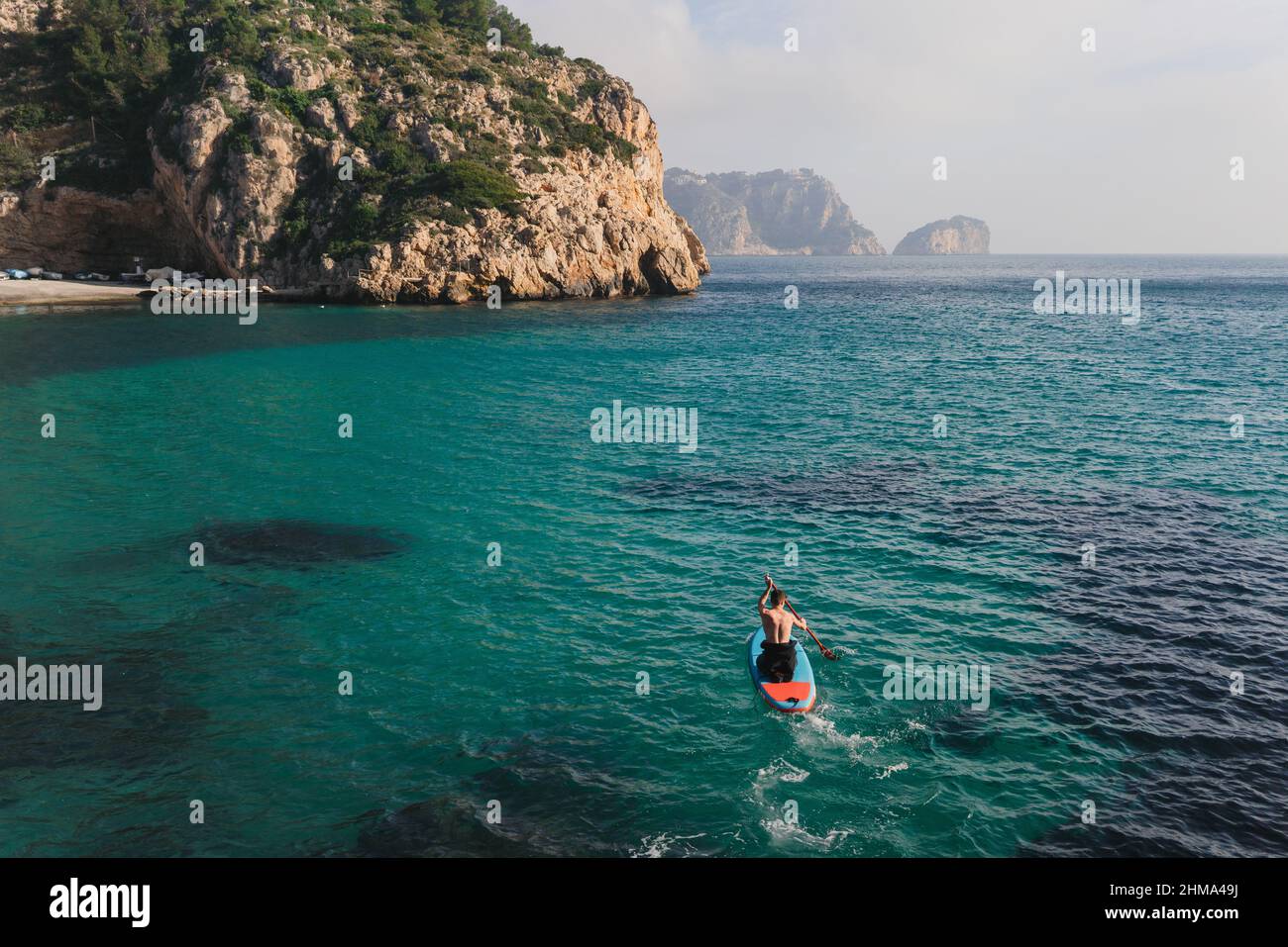 Vue latérale d'une femelle anonyme en chapeau assis dans la roche regardant le trou dans le plafond de la grotte près de la mer le jour ensoleillé à Algarve, Portugal Banque D'Images