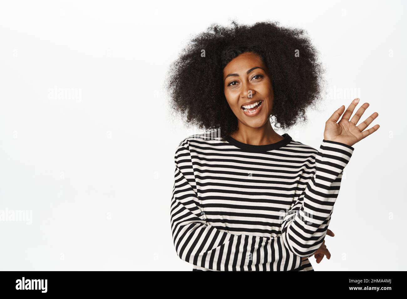 Une femme afro-américaine amicale vous saluant, se portant la main à l'appareil photo, vous saluant, dites bonjour, souriante et insouciante à l'appareil photo, debout sur fond blanc Banque D'Images
