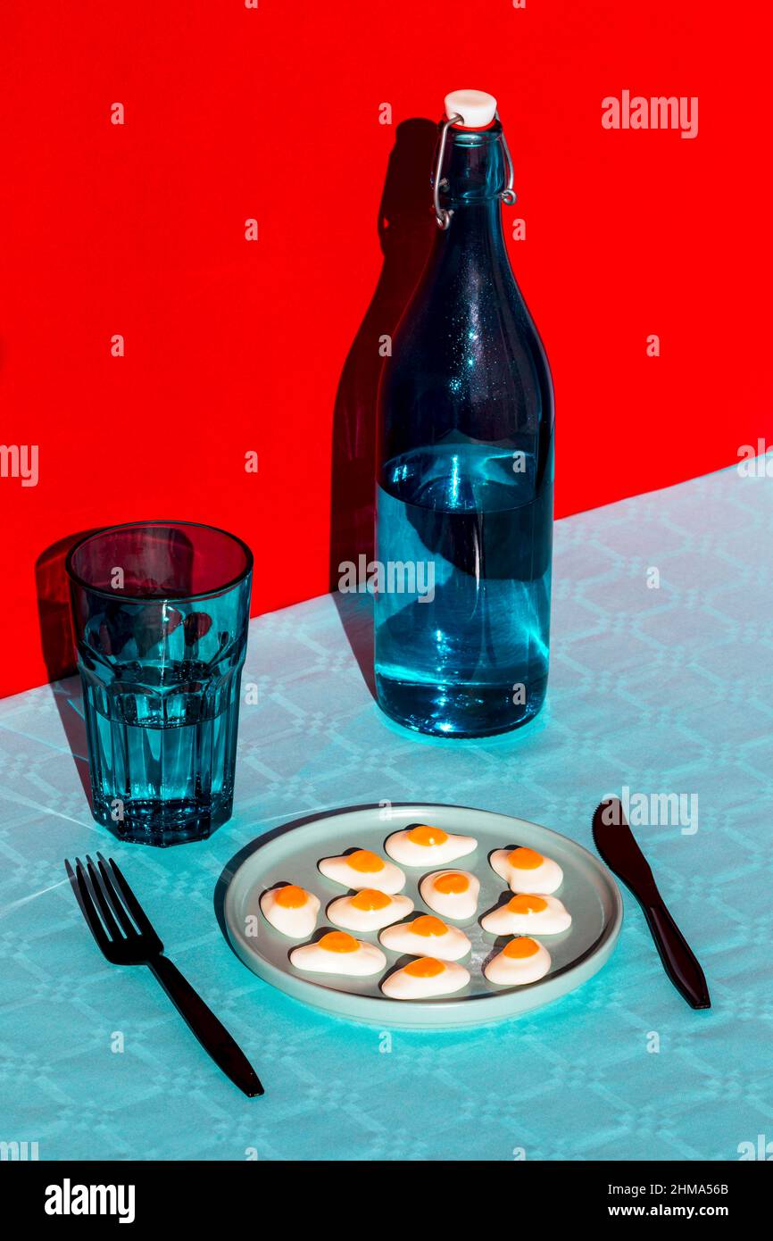 Par dessus la composition de la bouteille d'eau avec le verre face plaque avec les oeufs bouillis en deux et fourchette et couteau placés sur la surface bleue contre b rouge Banque D'Images