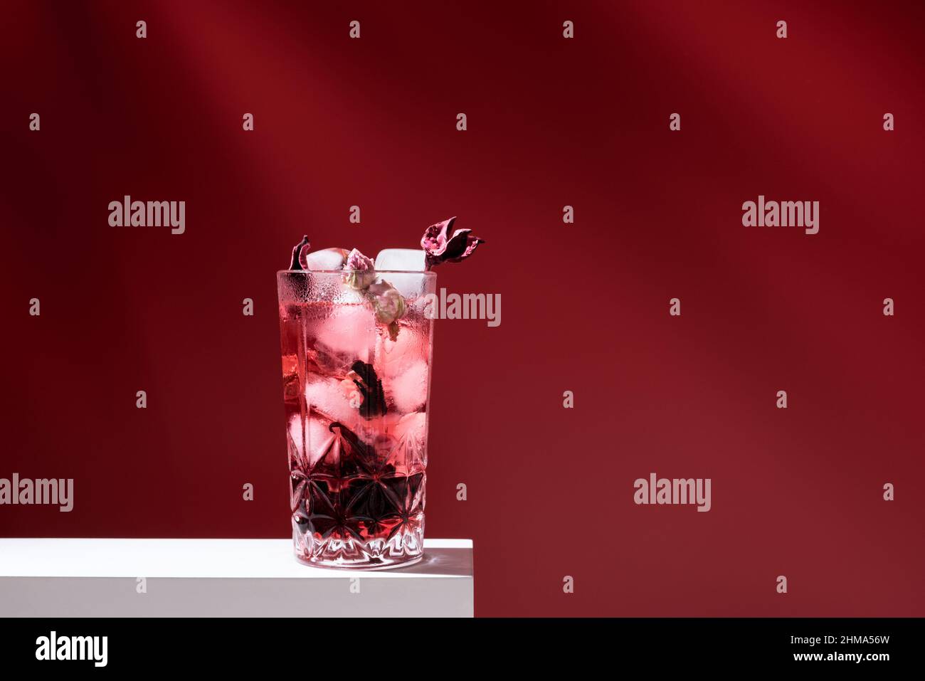 Composition de verre rempli de gin tonique rose et de glace placée sur une table blanche sur fond rouge Banque D'Images