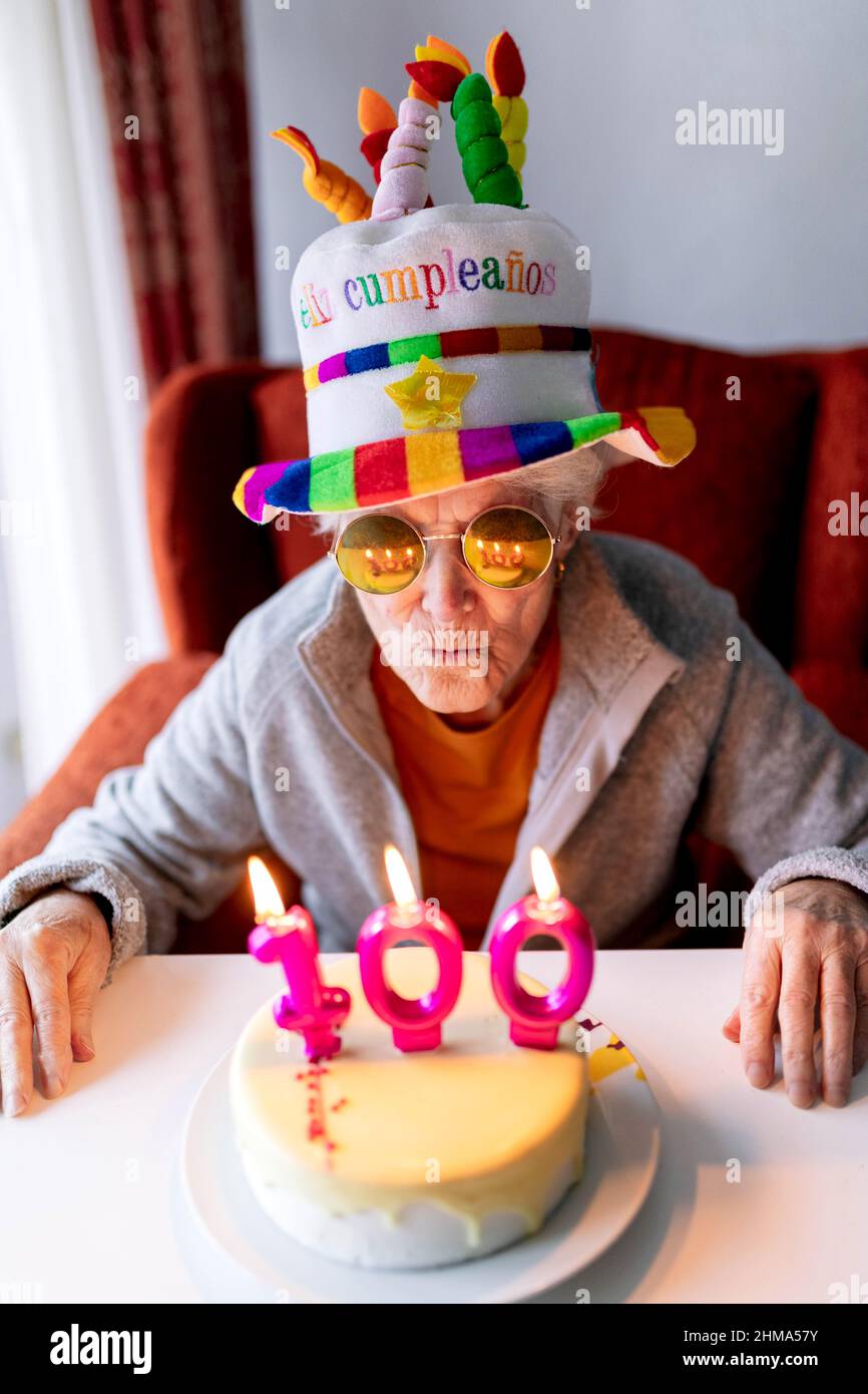 Femme Agee Dans Un Chapeau Amusant Et Des Lunettes De Soleil Soufflant Des Bougies Allumees Numero 100 Sur Le Gateau D Anniversaire Et Celebrant L Anniversaire A La Maison Photo Stock Alamy