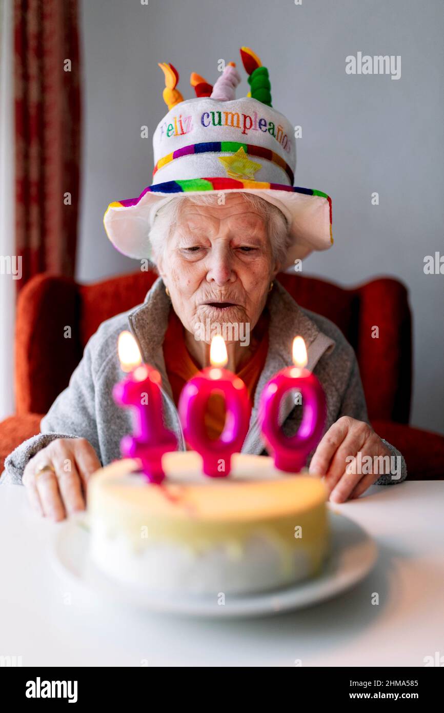 Femme âgée dans un chapeau drôle soufflant des bougies de combustion avec  le numéro 100 sur le gâteau d'anniversaire et célébrant l'anniversaire à la  maison Photo Stock - Alamy