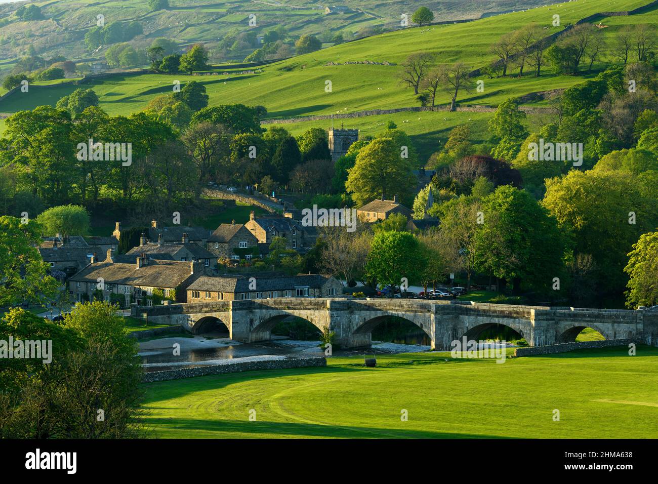 Pittoresque et ensoleillé Burnsall niché dans la vallée (pont de 5 arcades, cottages attrayants, tour d'église, champs verdoyants à flanc de colline) - Yorkshire Dales, Angleterre, Royaume-Uni. Banque D'Images