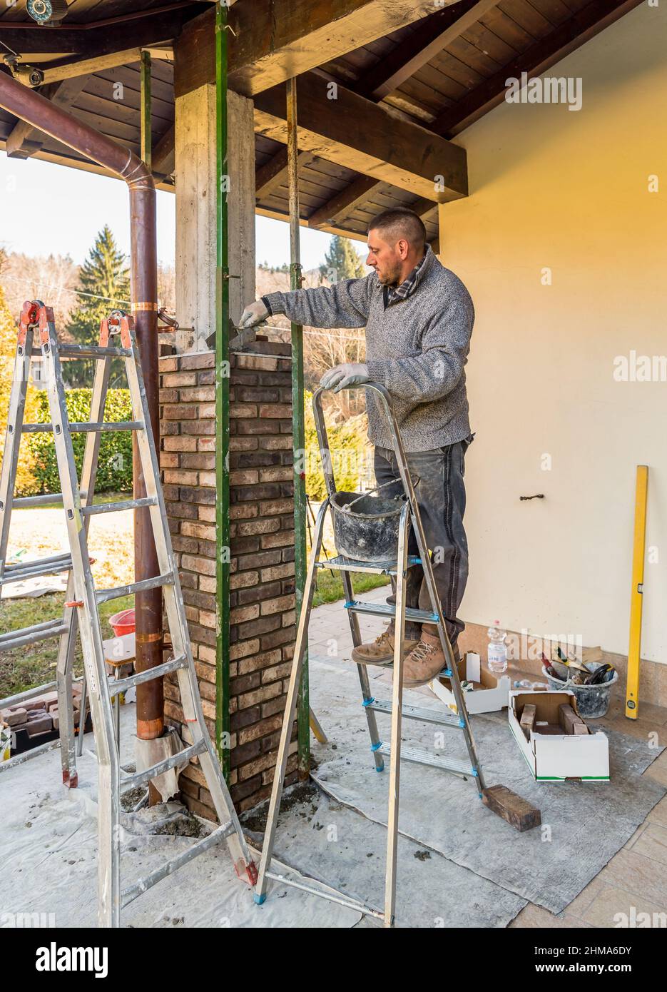 Bricklayer travailleur installant des briques sur le pilier extérieur en béton de la maison. Ouvrier de construction posant des briques. Banque D'Images