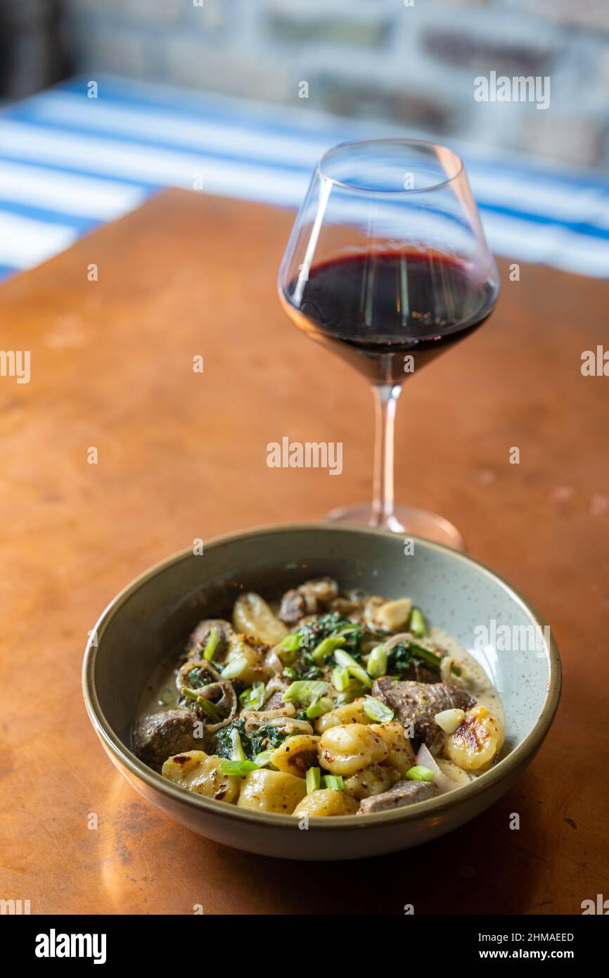 Un bol de gnocchi avec steak servi avec un verre de vin rouge Banque D'Images