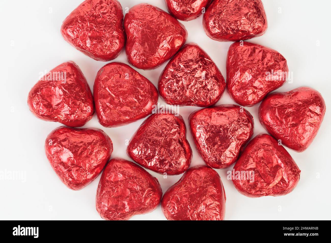 Bonbons au chocolat en forme de coeur enveloppés de papier d'aluminium rouge. Il est situé sur une surface blanche. Gros plan. Banque D'Images