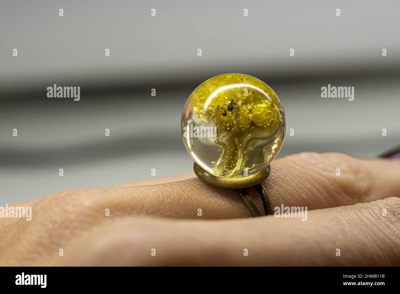 Gros plan d'un anneau en résine époxy sur le doigt d'une femelle - fleurs jaunes séchées dans un morceau de bijoux Banque D'Images