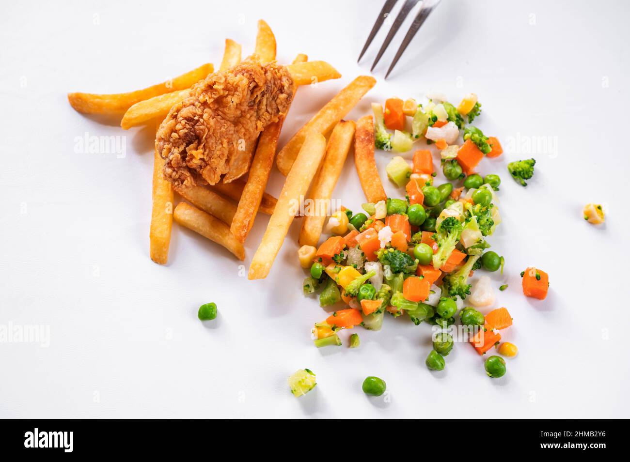 Un morceau de viande de poulet frite en flocons de maïs, frites et légumes ( pois, carottes, maïs, chou-fleur et brocoli) éparpillés sur fond blanc, p Banque D'Images