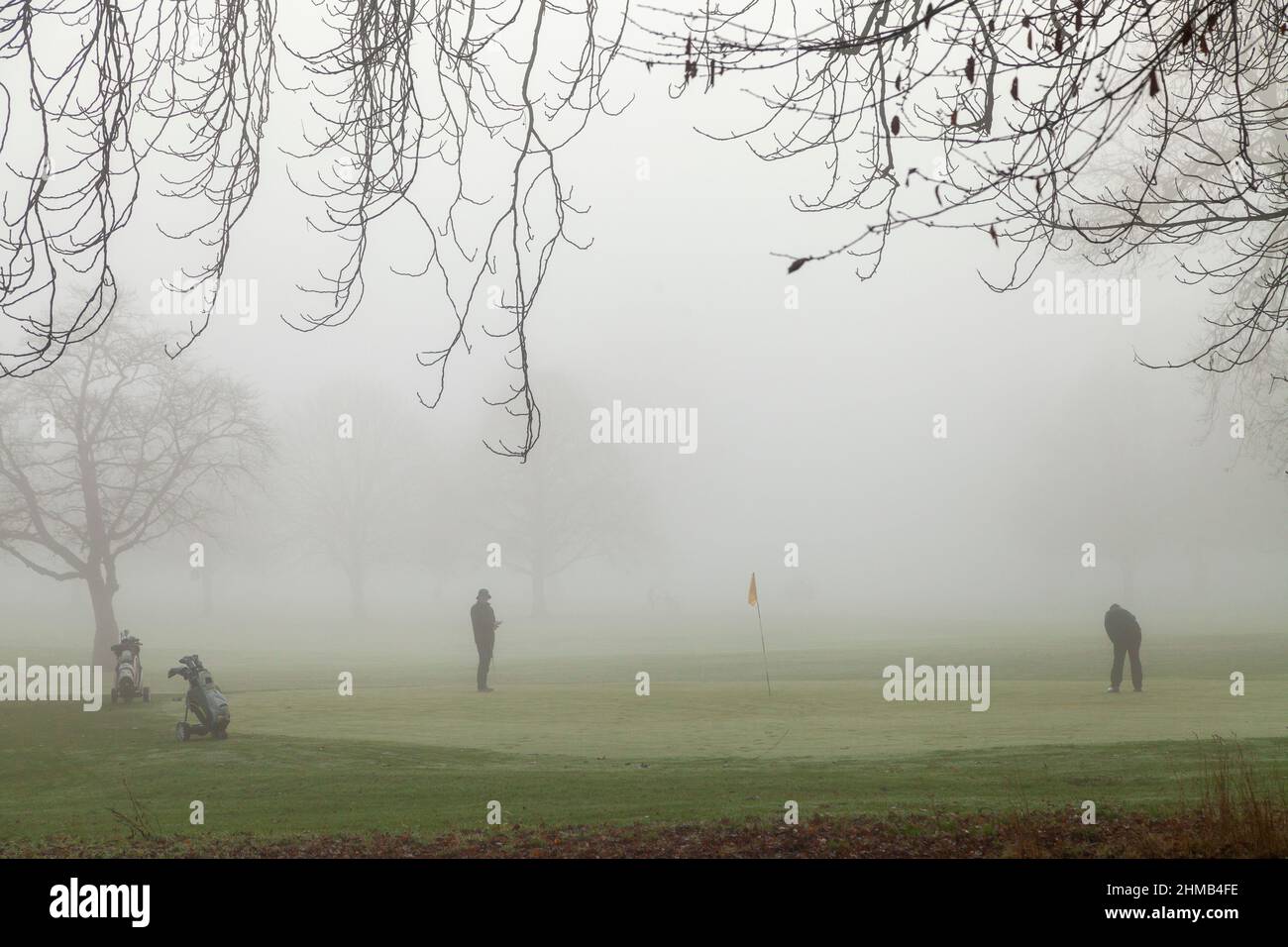 Deux golfeurs sur un vert d'exercice dans la brume épaisse, North inch, Perth, Ecosse Banque D'Images