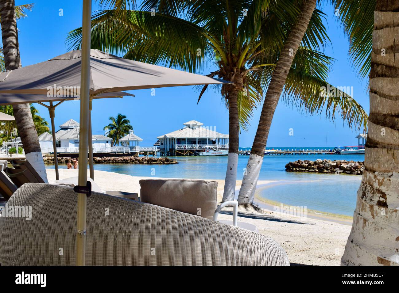 Une journée idyllique dans une station balnéaire sur la côte est de San Pedro, Belize avec un coin salon, palmiers, jetée, et 2 touristes dans l'eau. Banque D'Images