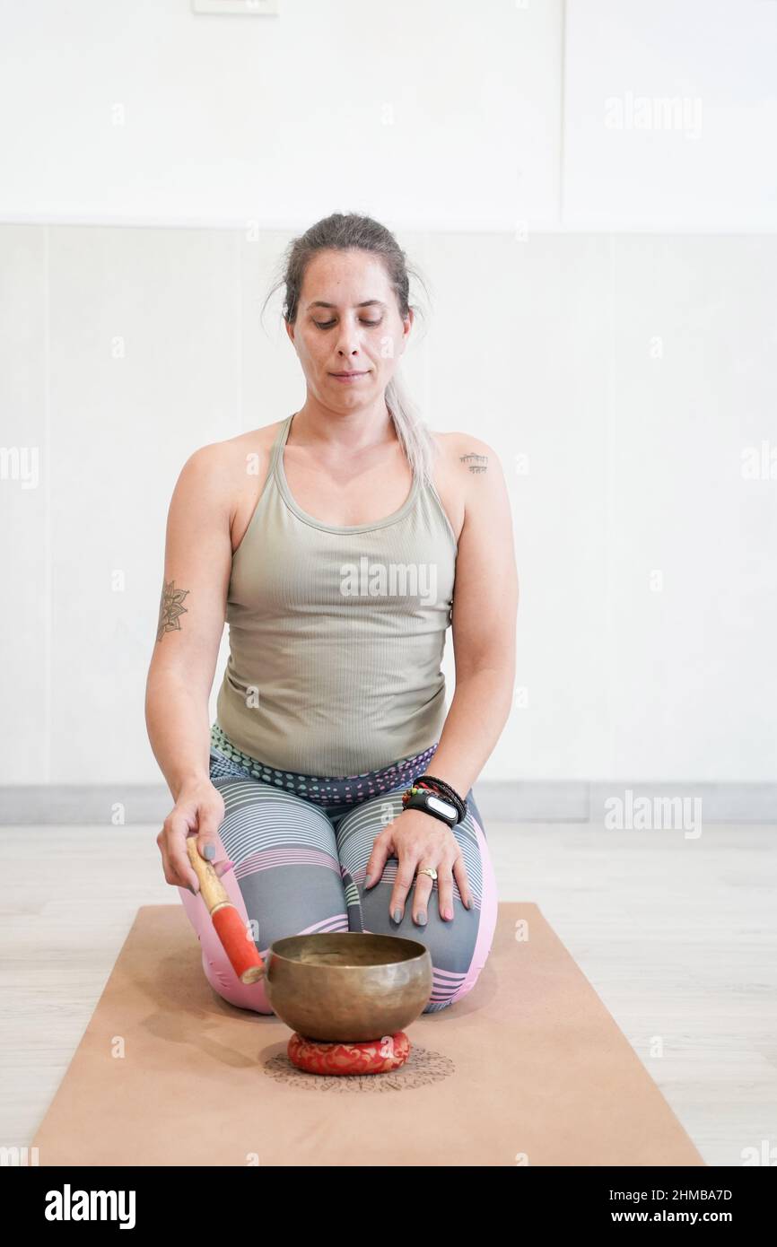 Femme athlète en posture de yoga Virasana ou héros pose jouant un bol de chant tibétain. Banque D'Images