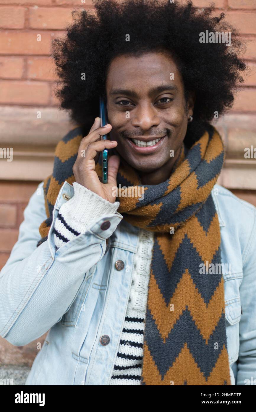 Portrait d'un homme afro-américain souriant avec un look moderne et une coiffure afro parlant au téléphone à l'extérieur. Banque D'Images