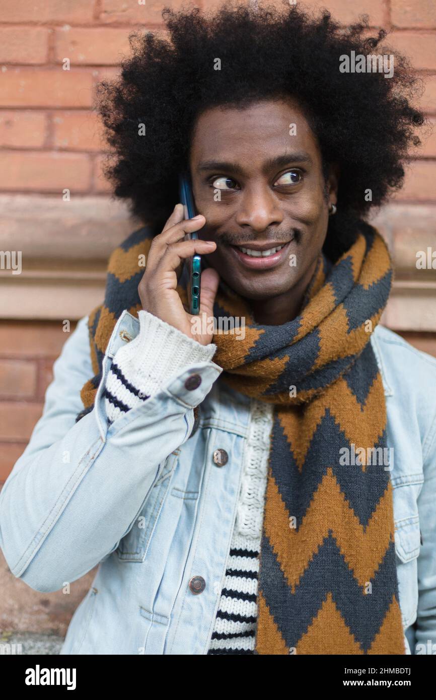 Portrait d'un jeune Africain américain avec une coiffure afro et des vêtements à la mode parlant au téléphone en extérieur. Banque D'Images