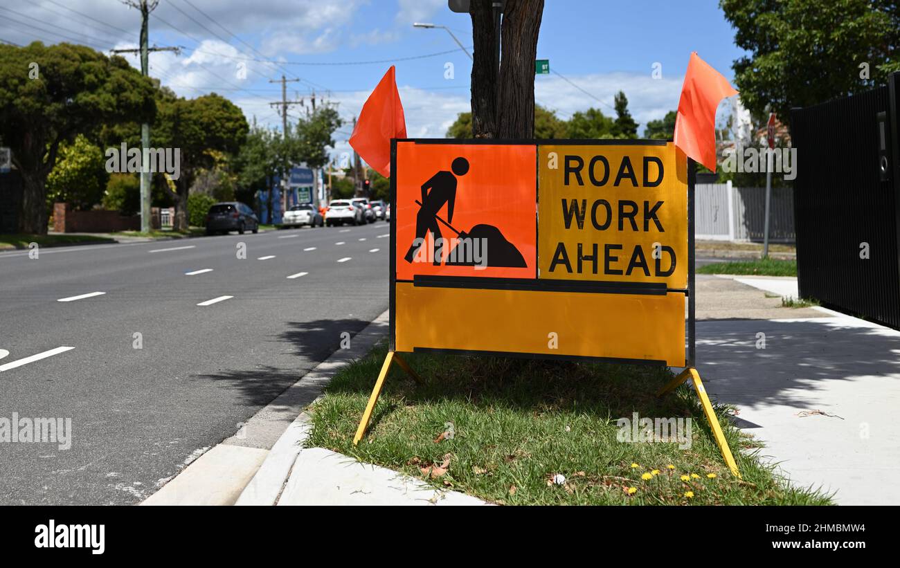 Panneau Road Work Ahead, avec deux petits drapeaux orange, à côté d'une route par beau temps Banque D'Images