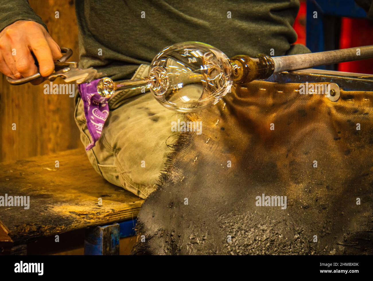 souffleur de verre formant un gobelet de verre sur ses genoux lorsqu'il est chaud Banque D'Images