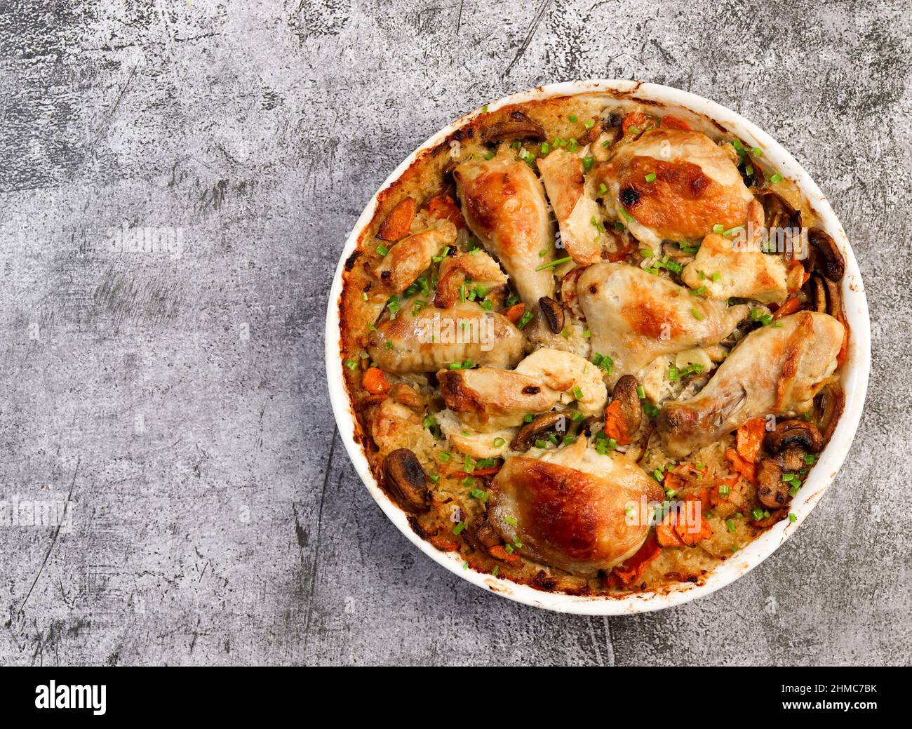 Poulet et riz cuits au four avec oignons, carottes et herbes dans un plat blanc sur fond gris foncé. Vue de dessus, plan d'appartement Banque D'Images