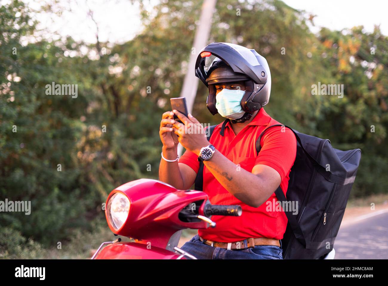 Jeune indien délivaire garçon avec masque médical de recherche adresse sur téléphone mobile en utilisant la carte ou la navigation - concept de la technologie , service de livraison Banque D'Images