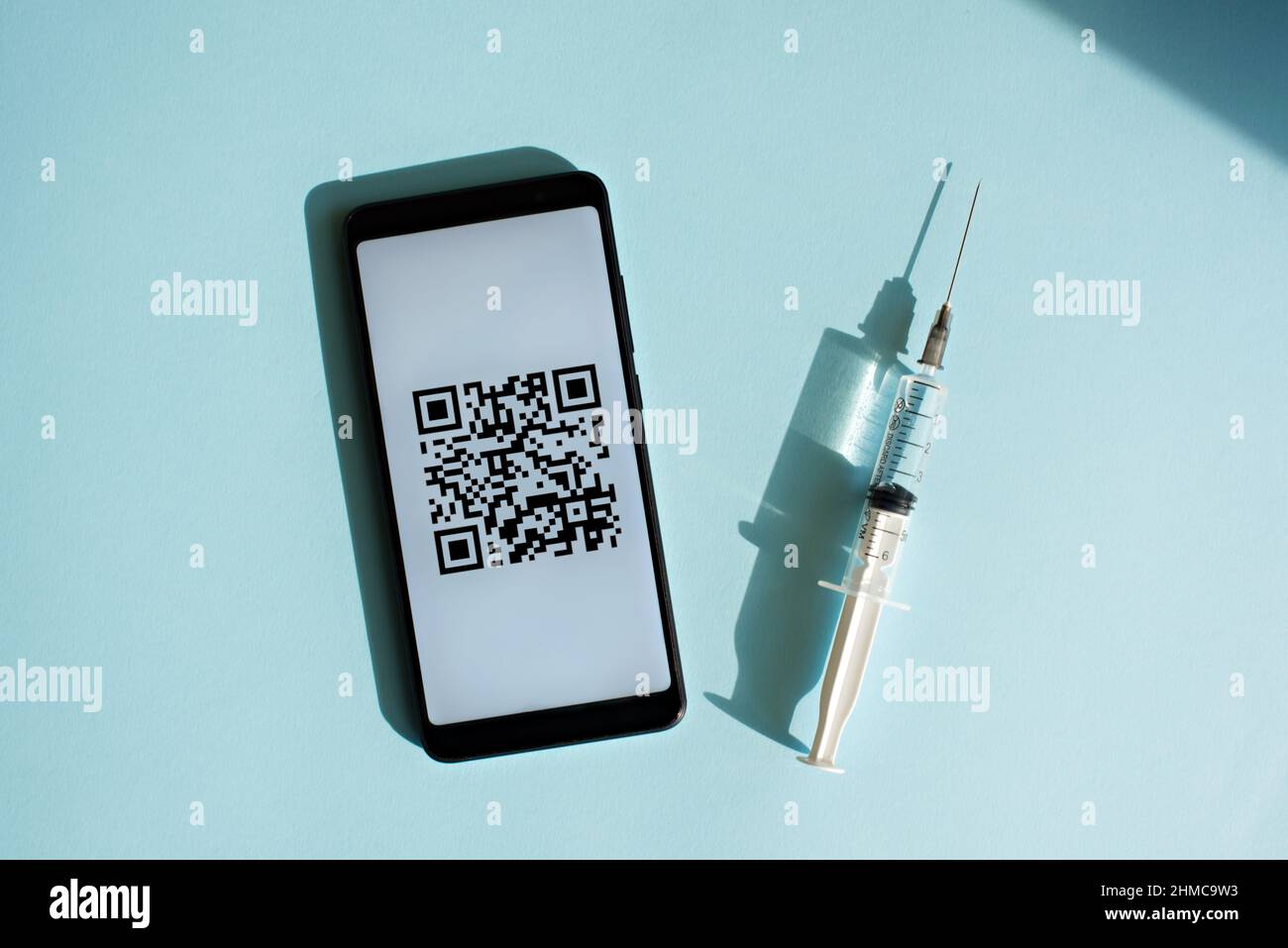 Smartphone avec code quar du certificat de vaccination sur l'écran, seringue et masque médical sur fond bleu clair. Banque D'Images