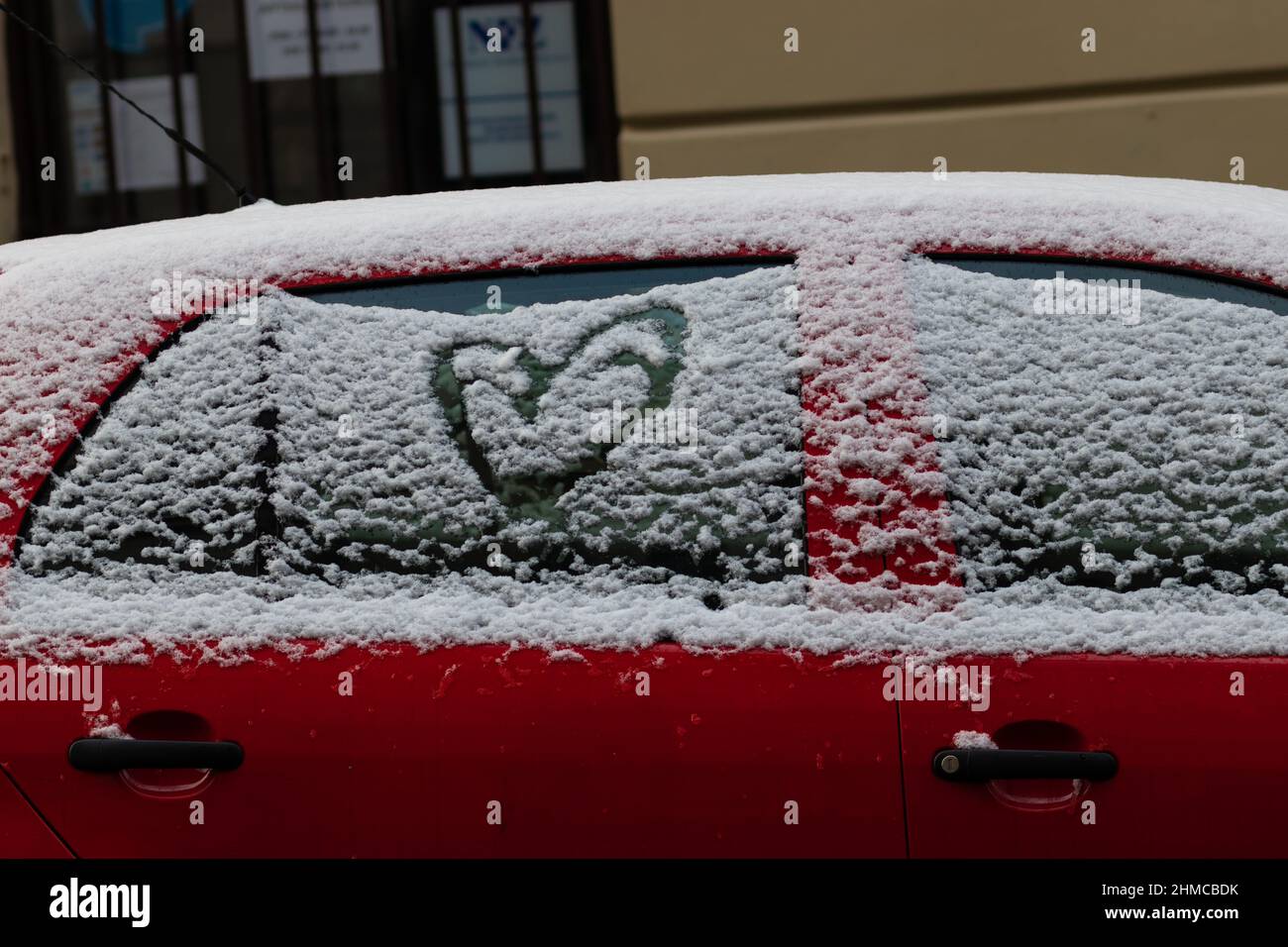 Un coeur peint par la neige, sur la fenêtre d'une voiture rouge recouverte de neige Banque D'Images