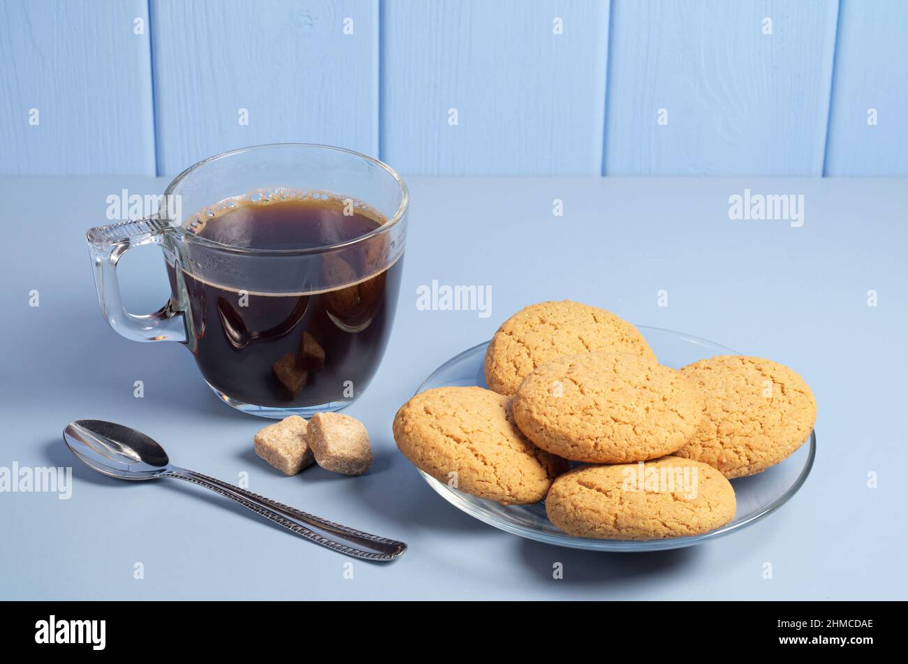 Biscuits aux flocons d'avoine et tasse de café chaud dans des plats transparents sur table bleue Banque D'Images