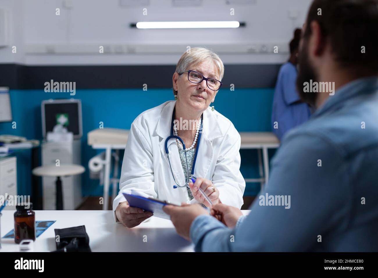 Femme médecin donnant des dossiers de presse-papiers à l'homme pour signer pour la paperasserie médicale. Médecin demandant au patient la signature sur les papiers de contrôle lors de la visite pour guérir la maladie. Personne signant les dossiers d'examen. Banque D'Images