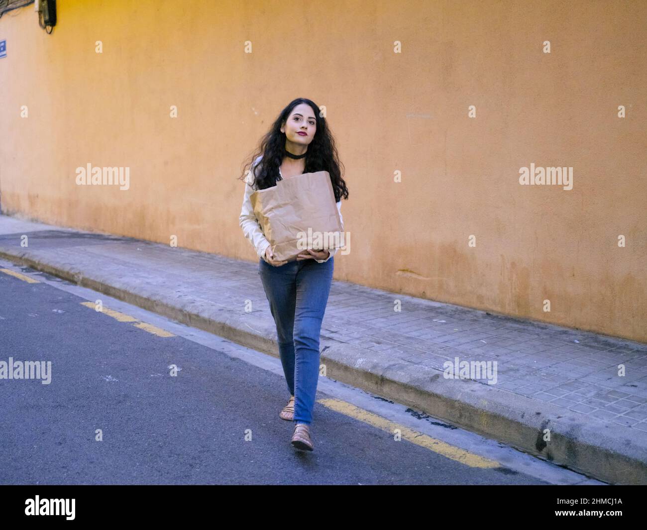 Une jeune femme portant un sac écologique traversant la rue et regardant la caméra. Banque D'Images