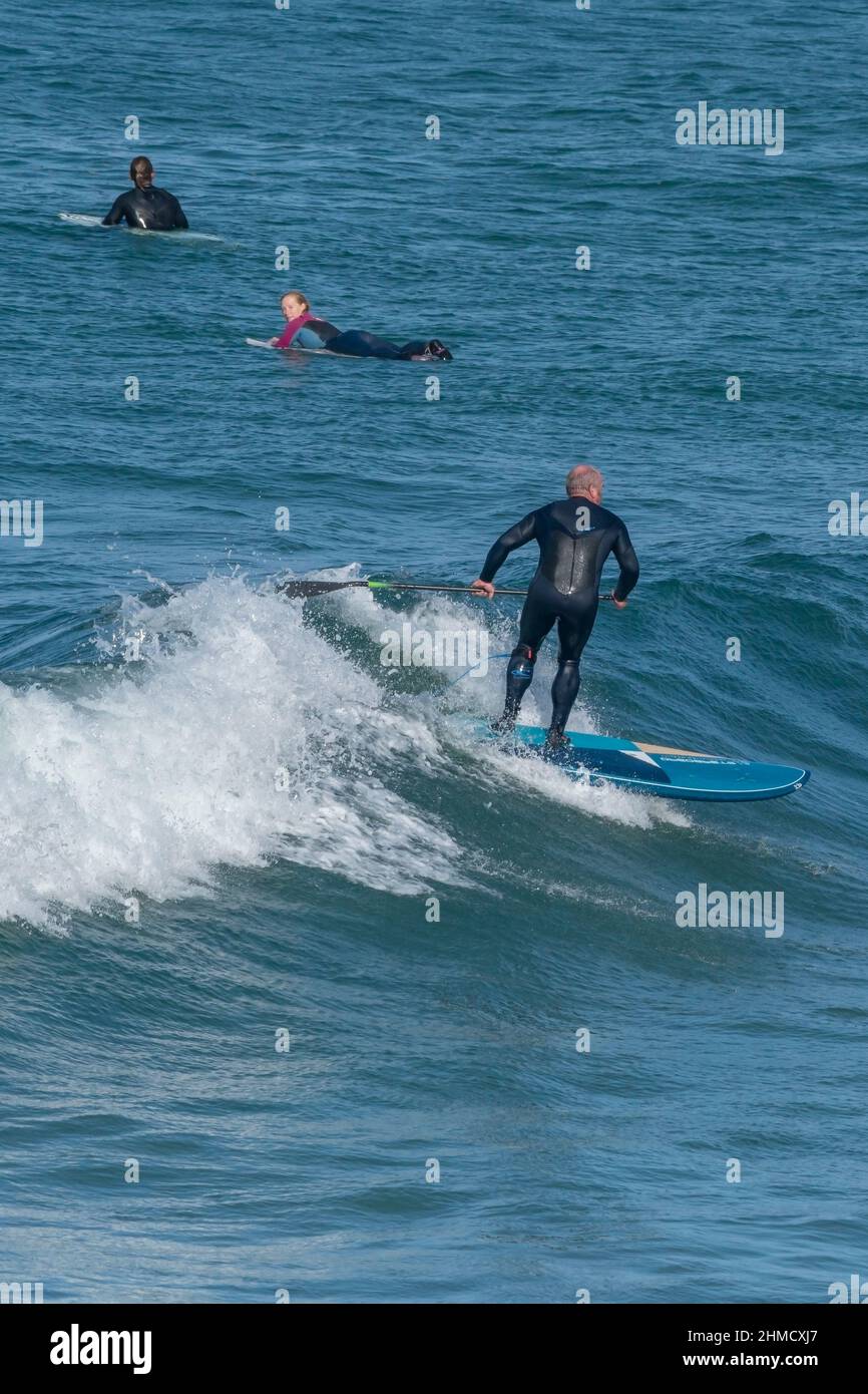 Un Paddleboarder debout et mature qui monte sur la crête d'une vague à Fistral à Newquay en Cornouailles. Banque D'Images