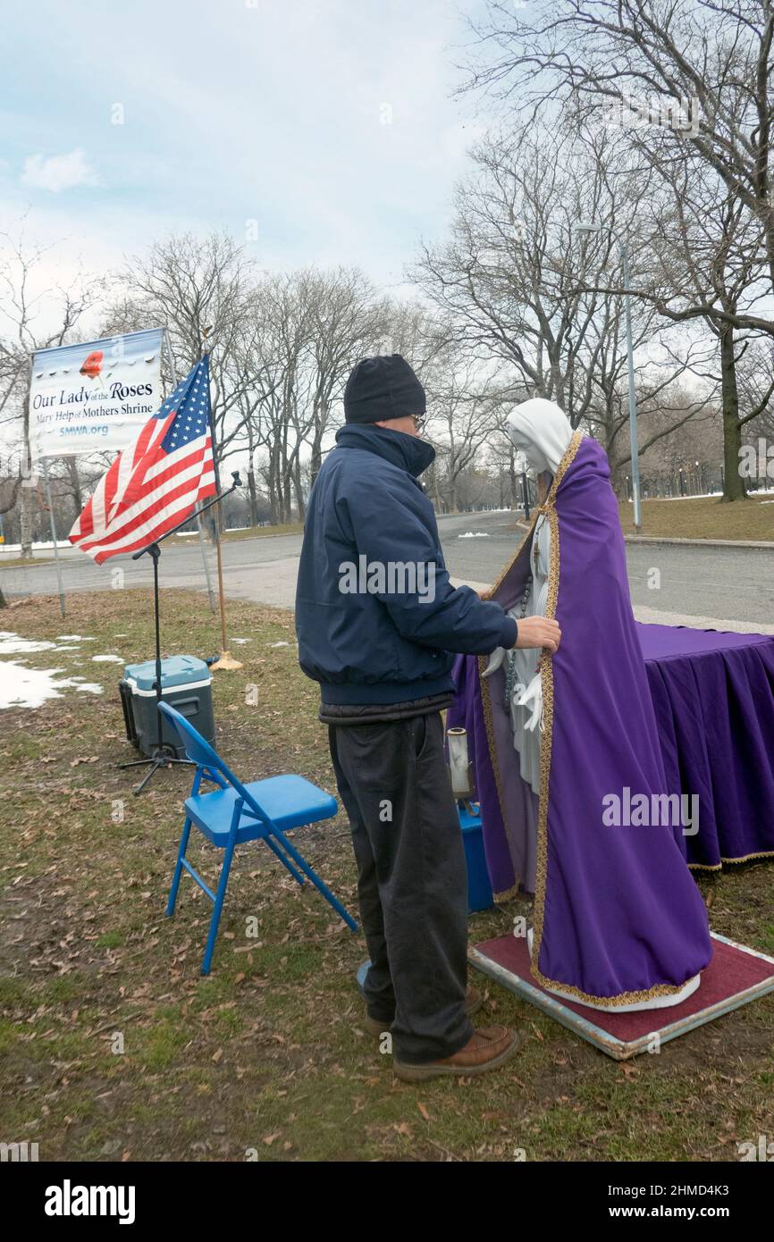 Un adorateur dévot habille une statue de la Vierge Marie avant un service de plein air dans un parc de Queens, New York. Banque D'Images