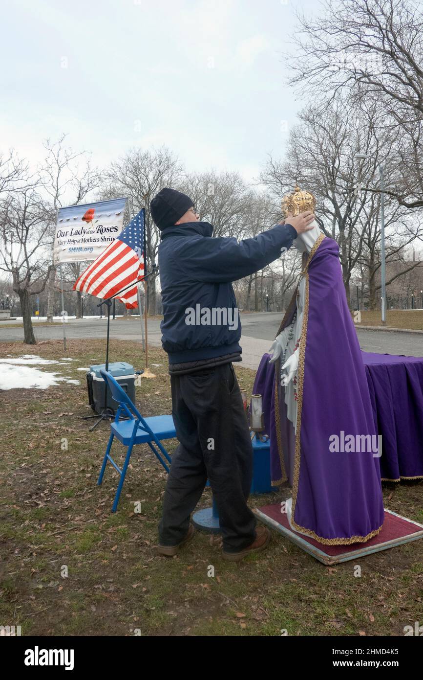 Un adorateur dévot habille une statue de la Vierge Marie avant un service de plein air dans un parc de Queens, New York. Banque D'Images