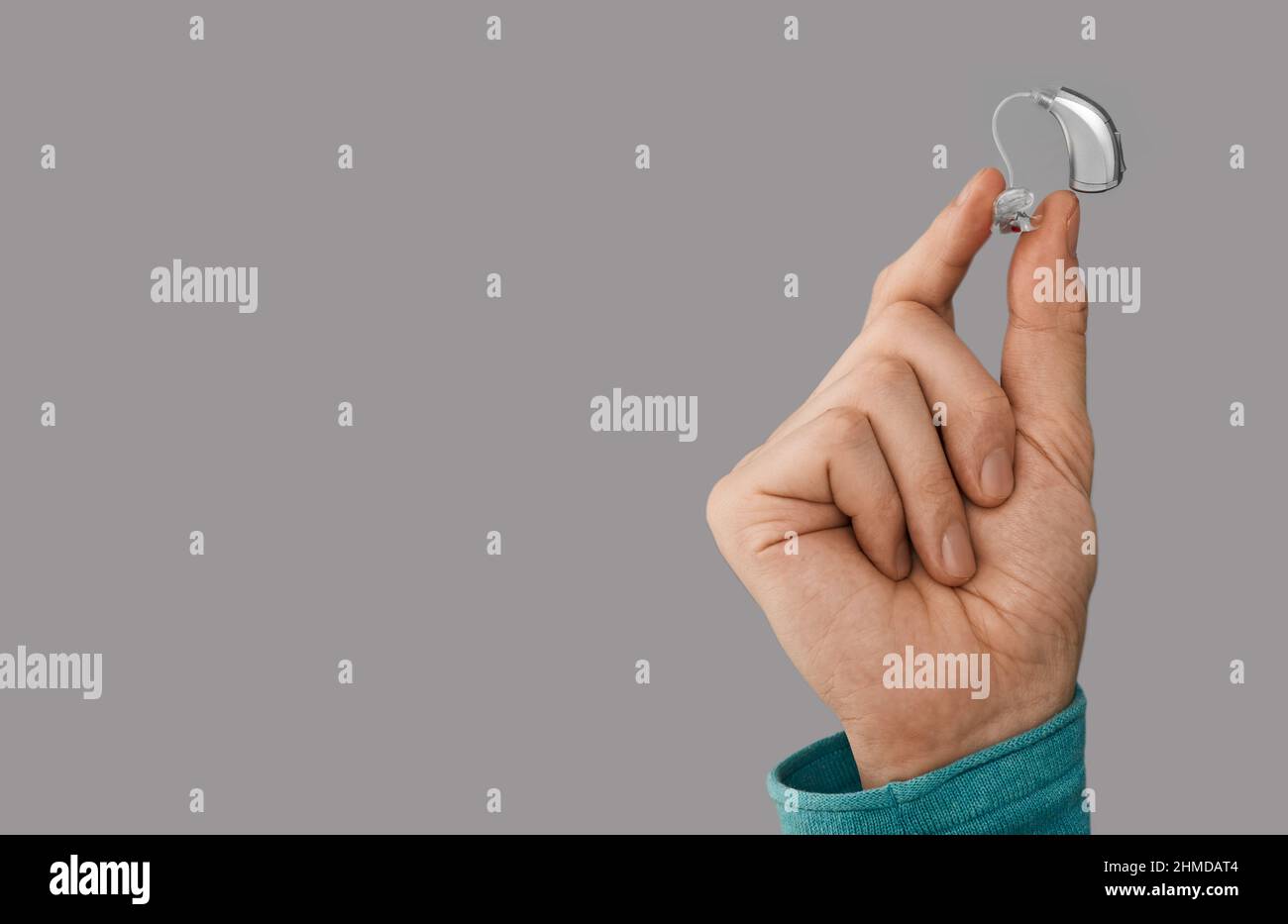 Aide auditive de main masculine, gros plan sur fond gris avec espace pour le texte. Solutions auditives, prothèses auditives BTE Banque D'Images