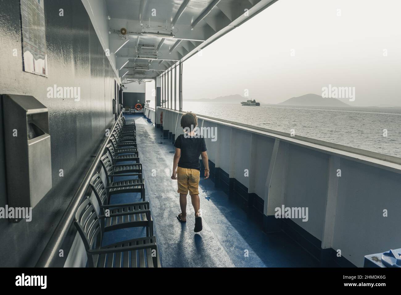 Garçon regardant vers la mer magnifique tout en marchant seul à côté des chaises sur le bateau de ferryboat Banque D'Images