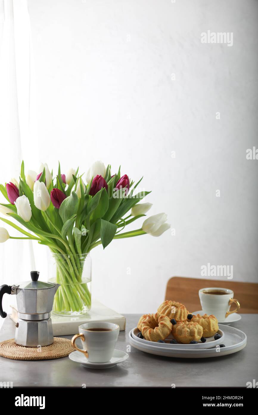 Petits gâteaux avec fruits sur assiette, tasse de café et bouquet de tulipes. Banque D'Images