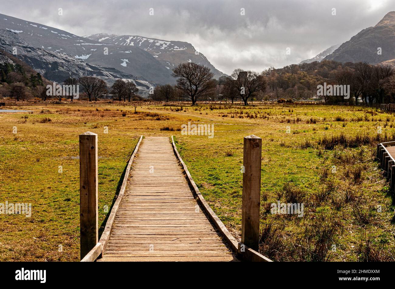 Une promenade ensoleillée à proximité de Llyn Padarn mène vers des montagnes accidentées avec des pistes enneigées et des sommets embrasés par des nuages gris tandis que des moutons s'embrassent à proximité Banque D'Images