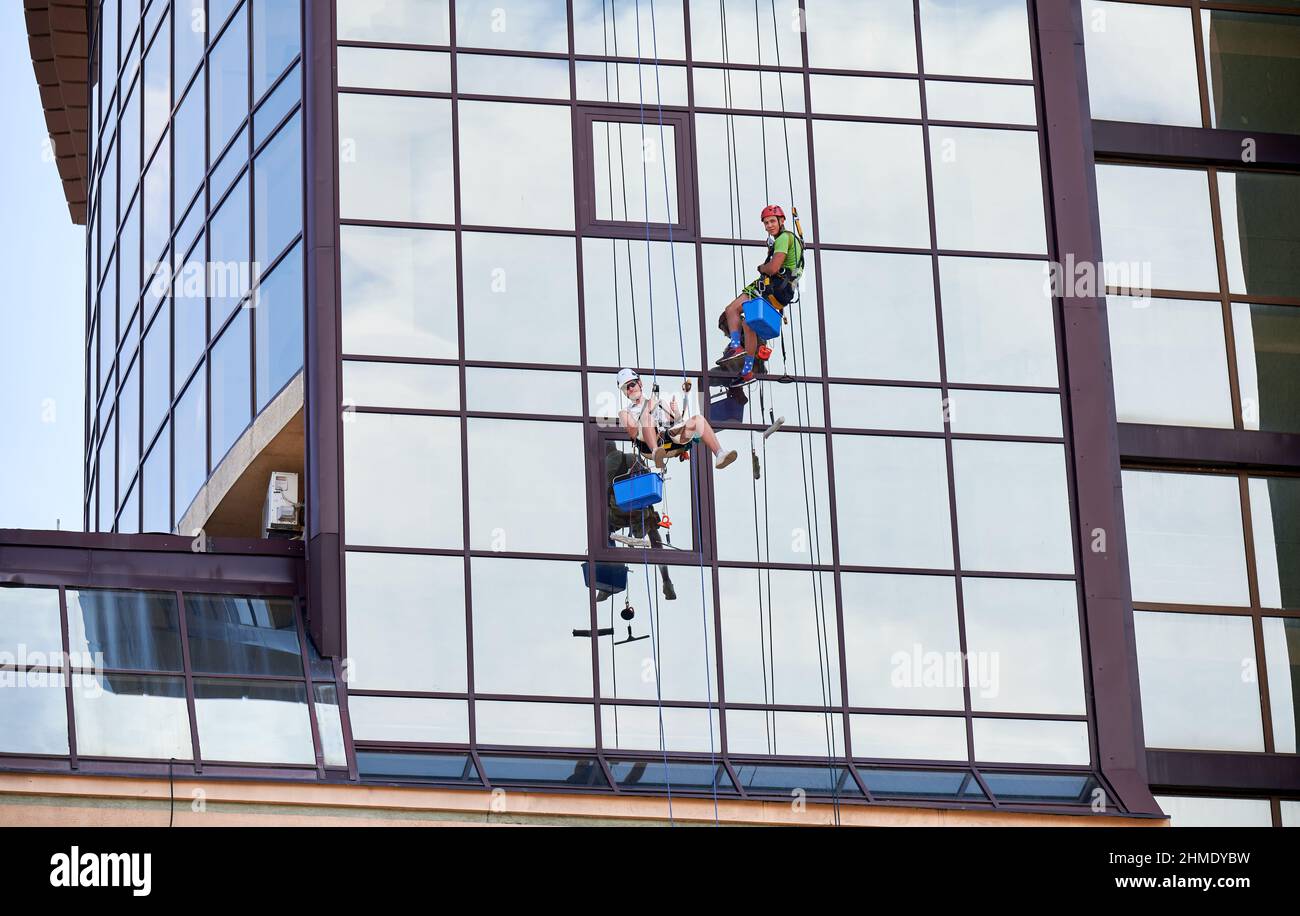 Ouvriers d'alpinisme industriel lavant des fenêtres en verre d'une tour de bâtiment, accrochés à des cordes d'escalade de sécurité. Deux nettoyeurs de fenêtre hommes travaillant ensemble à l'extérieur du gratte-ciel. Banque D'Images