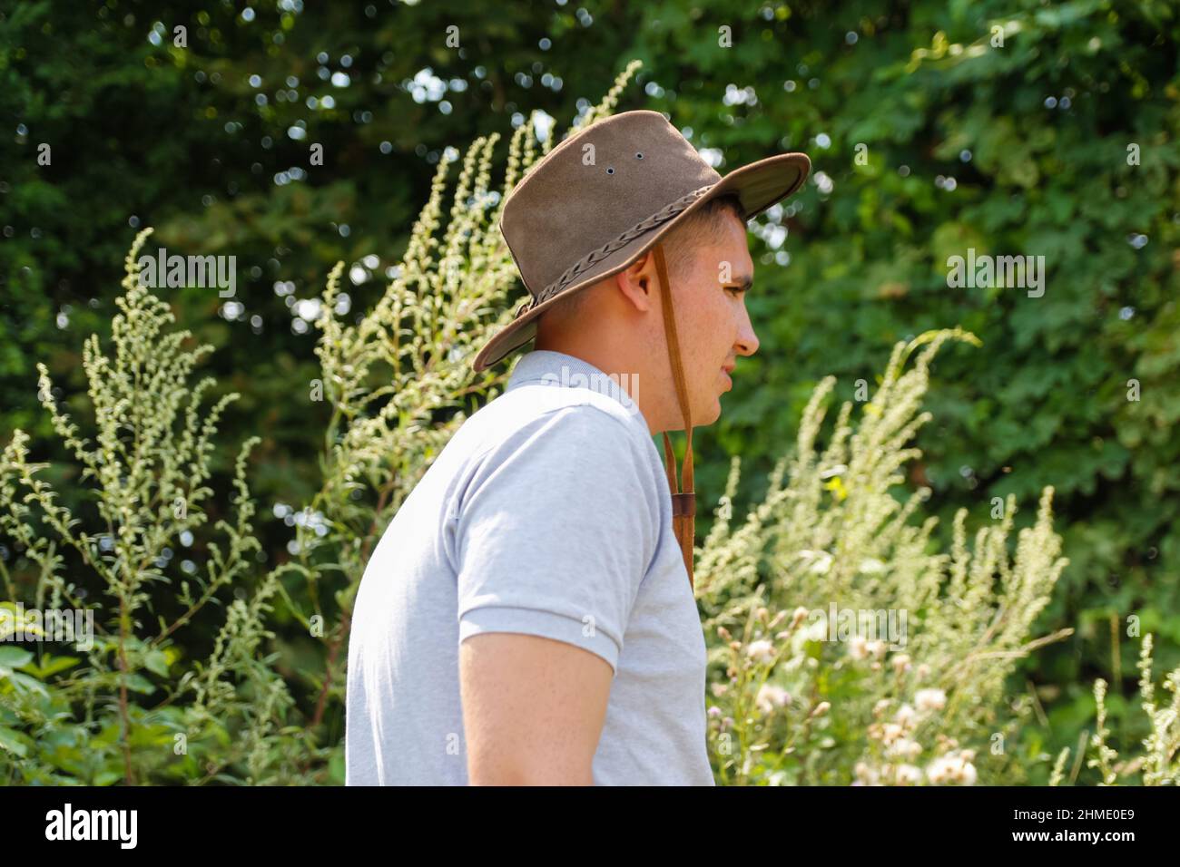 Homme en chapeau.Portrait d'un fermier souriant avec de l'herbe verte et de la nature des arbres en arrière-plan.Jeune homme portant un chapeau de cow-boy sur le terrain.Gros plan.Joyeux jeune p Banque D'Images