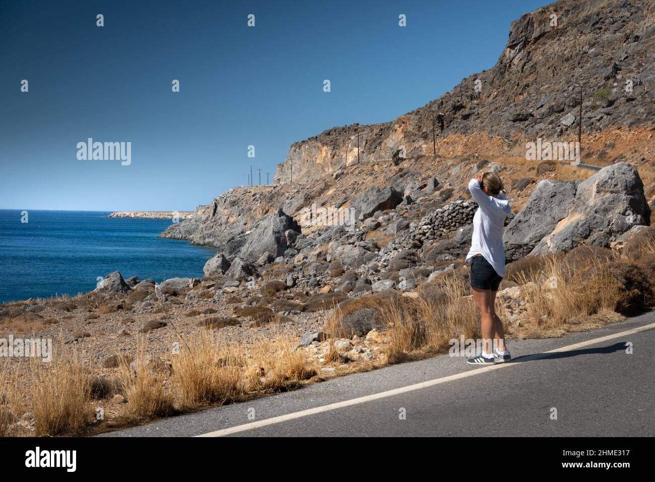 Femme debout à côté du marquage sur la route côtière asphaltée regardant la mer Banque D'Images