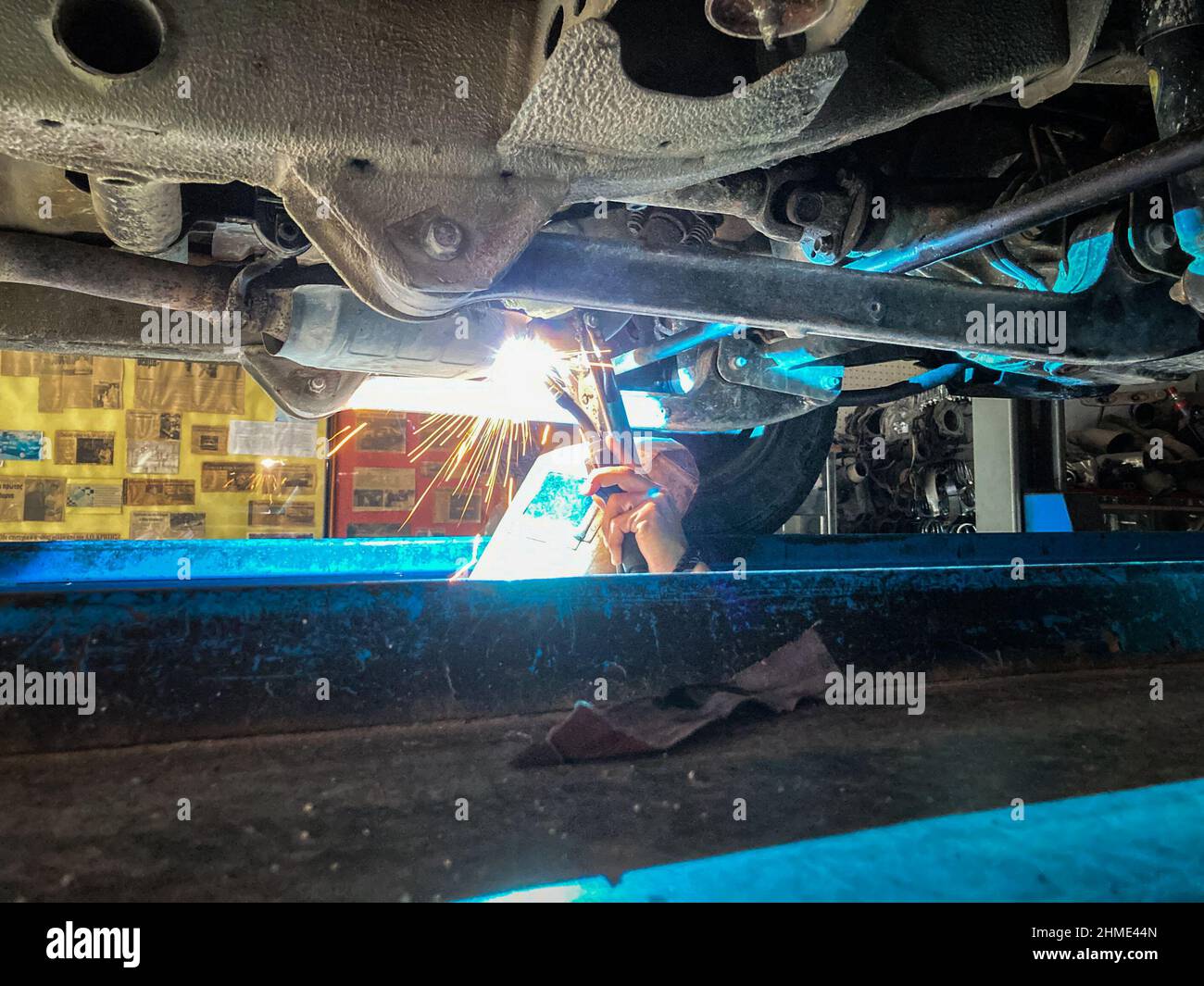 Un mécanicien soudeur soudant un tuyau d'échappement métallique avec des étincelles dans un atelier de réparation automobile Banque D'Images