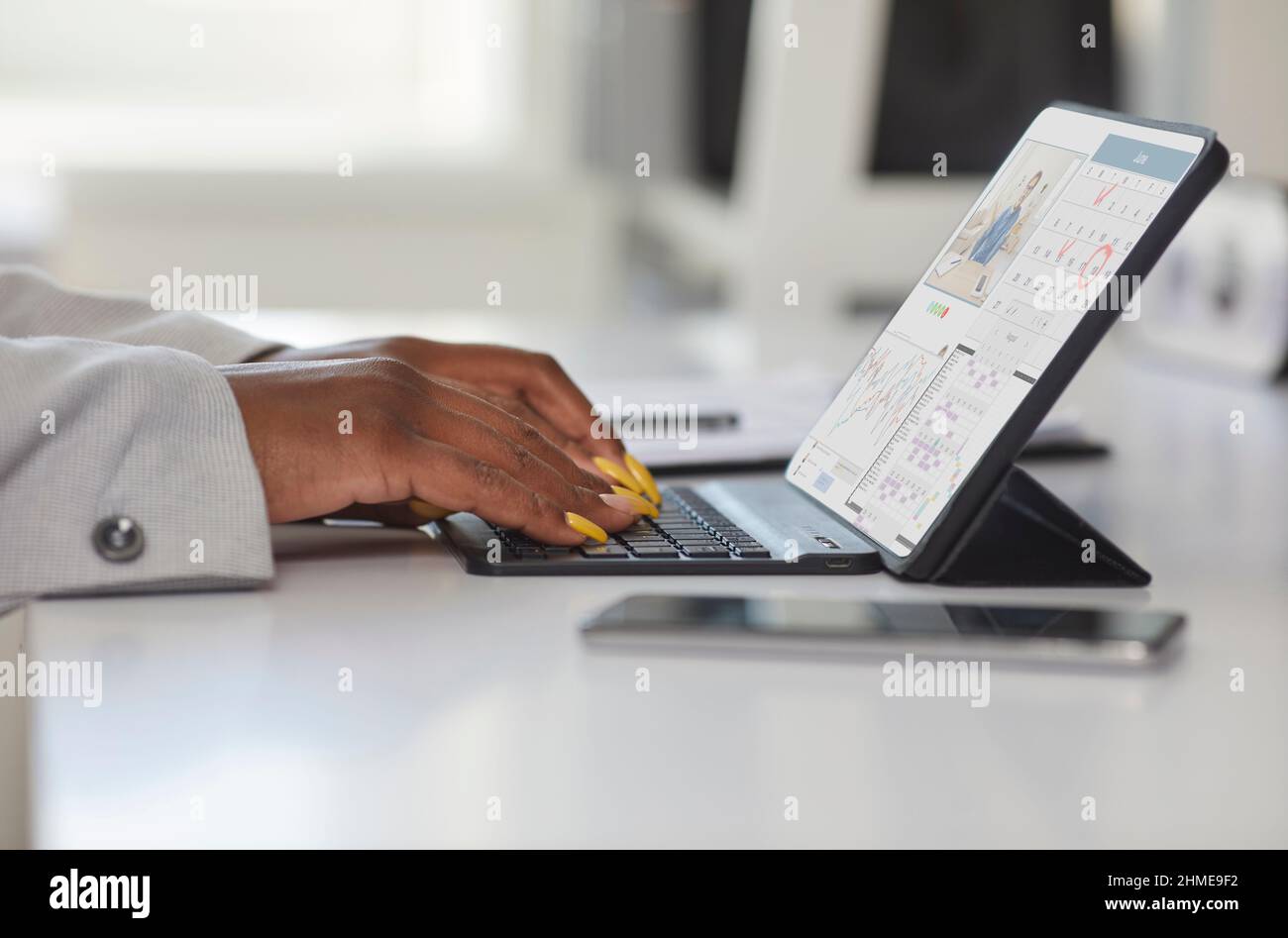 Femme noire assise à un bureau au bureau et dactylographiant sur le clavier de sa tablette Banque D'Images