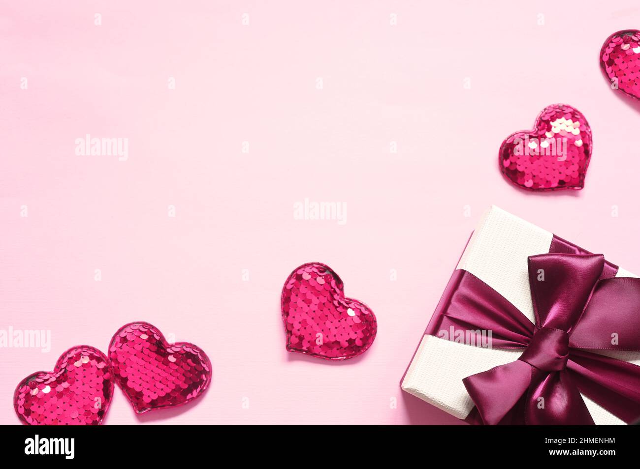 Vue du dessus photo des décorations de la Saint-Valentin. Boîte cadeau blanche avec noeud en ruban rose et petits coeurs sur fond rose isolé avec espace vide. Banque D'Images
