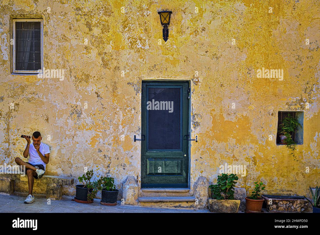 Un jeune homme écoute son téléphone portable devant la maison de Mdina Banque D'Images