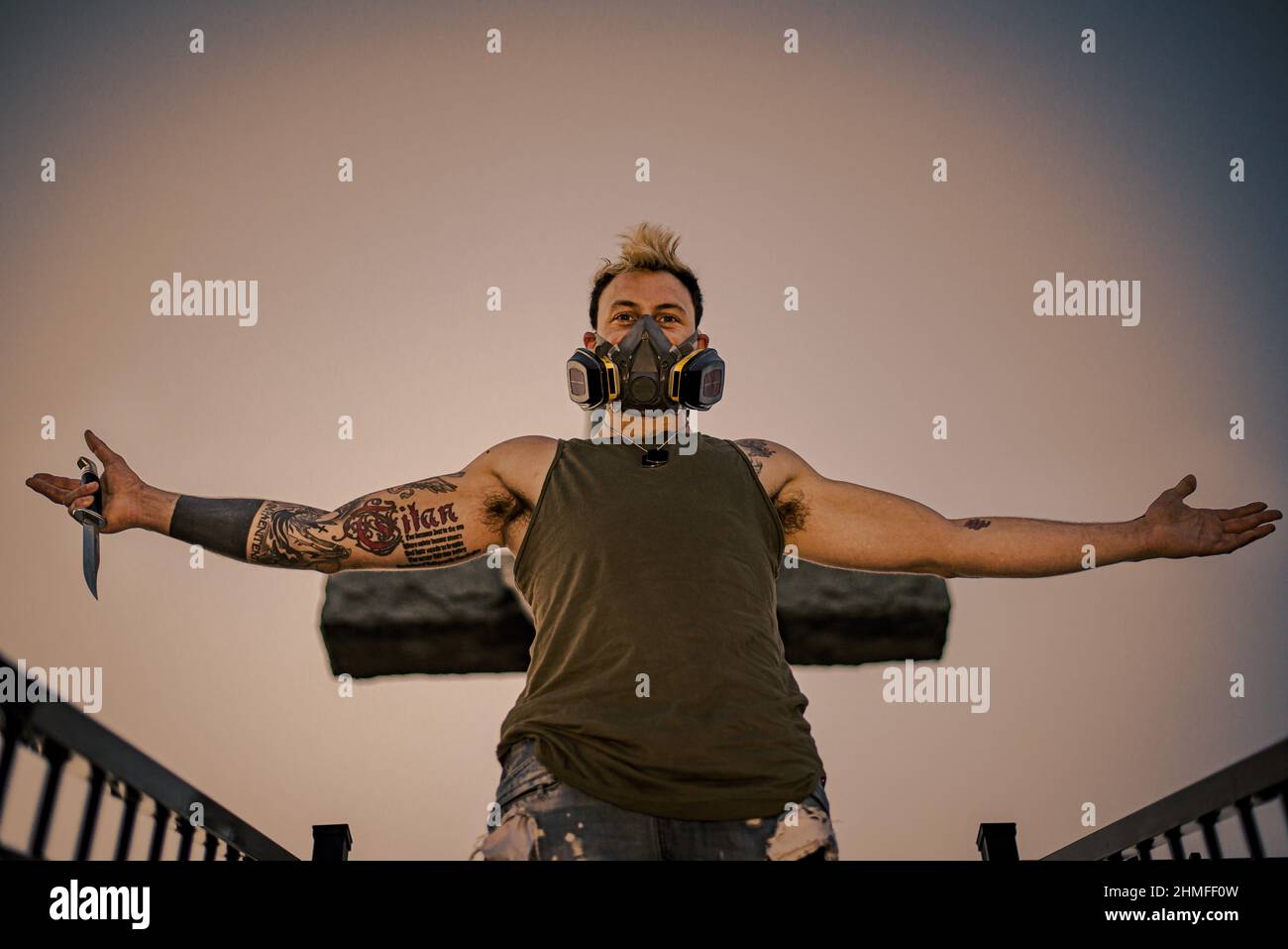 Jeune punk homme avec tatouages, masque et couteau, avec bras étirés, vue à angle bas Banque D'Images