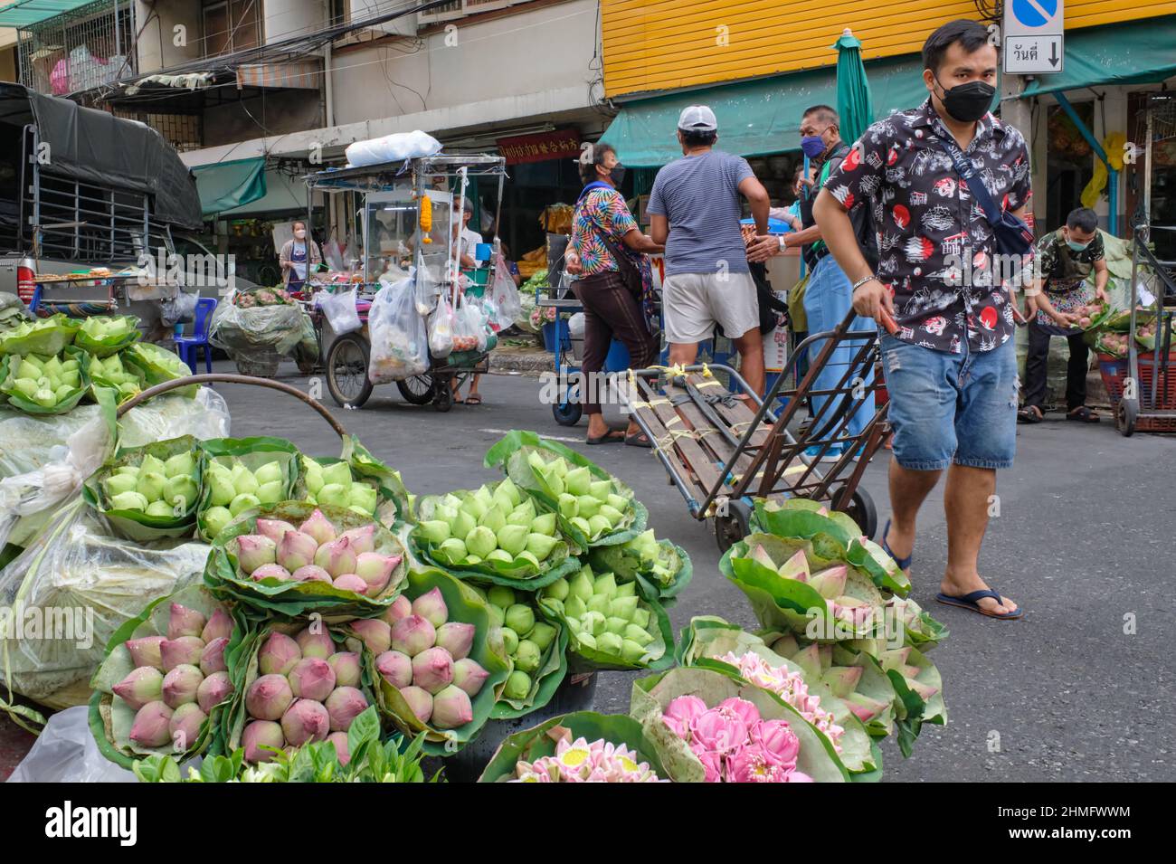 Un porteur avec son chariot passe devant une rue avec des bourgeons de lotus; à Pak Klong Talat, un marché connu pour son vaste éventail de fleurs, Bangkok, Thaïlande Banque D'Images