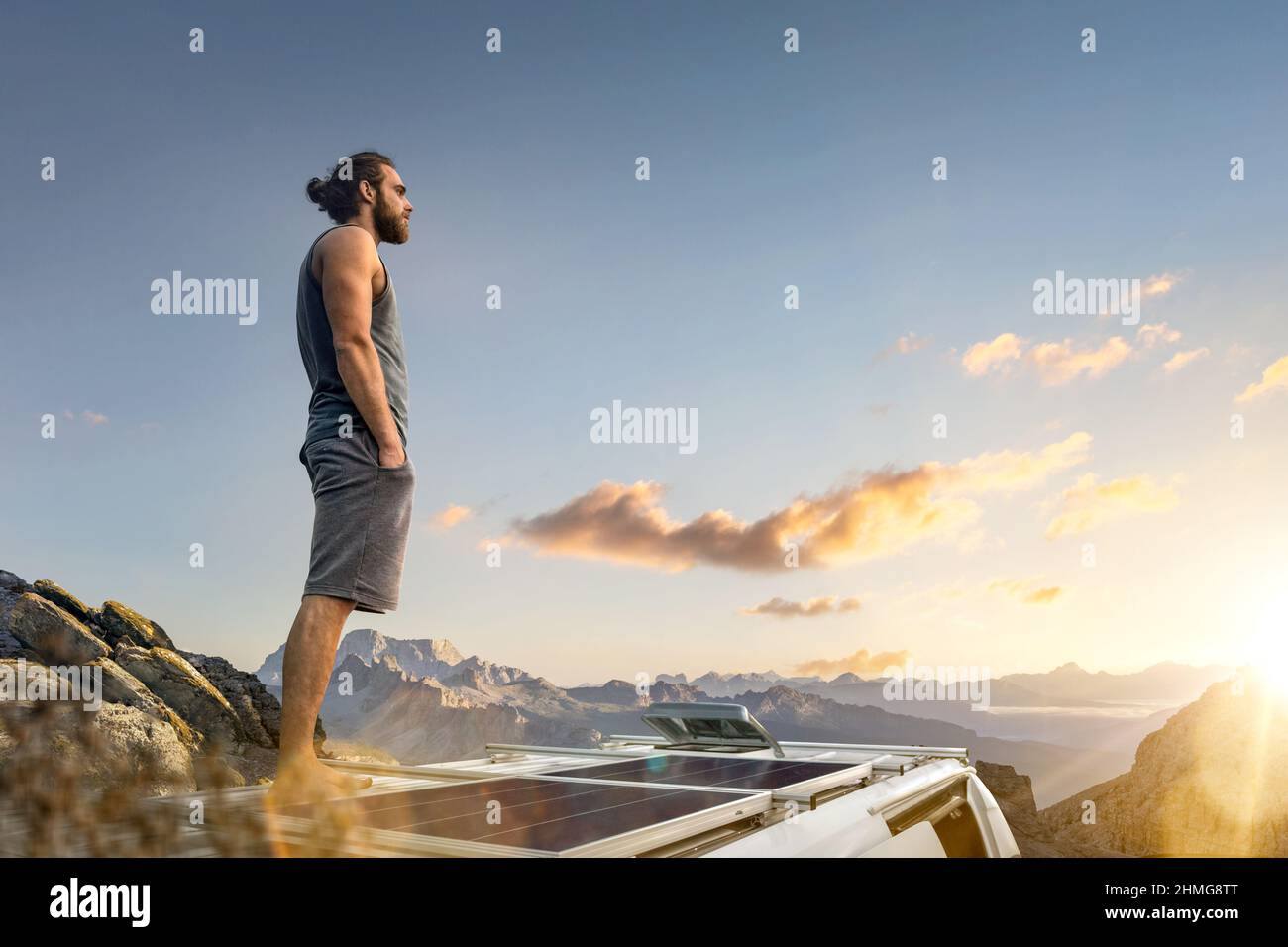 Homme debout sur le toit de sa camionnette de camping garée dans les montagnes Banque D'Images